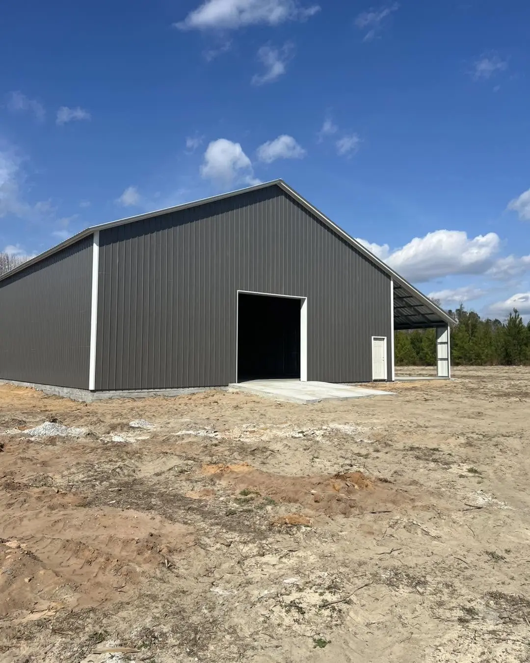 Gray steel building with a tall vehicle opening and side canopy