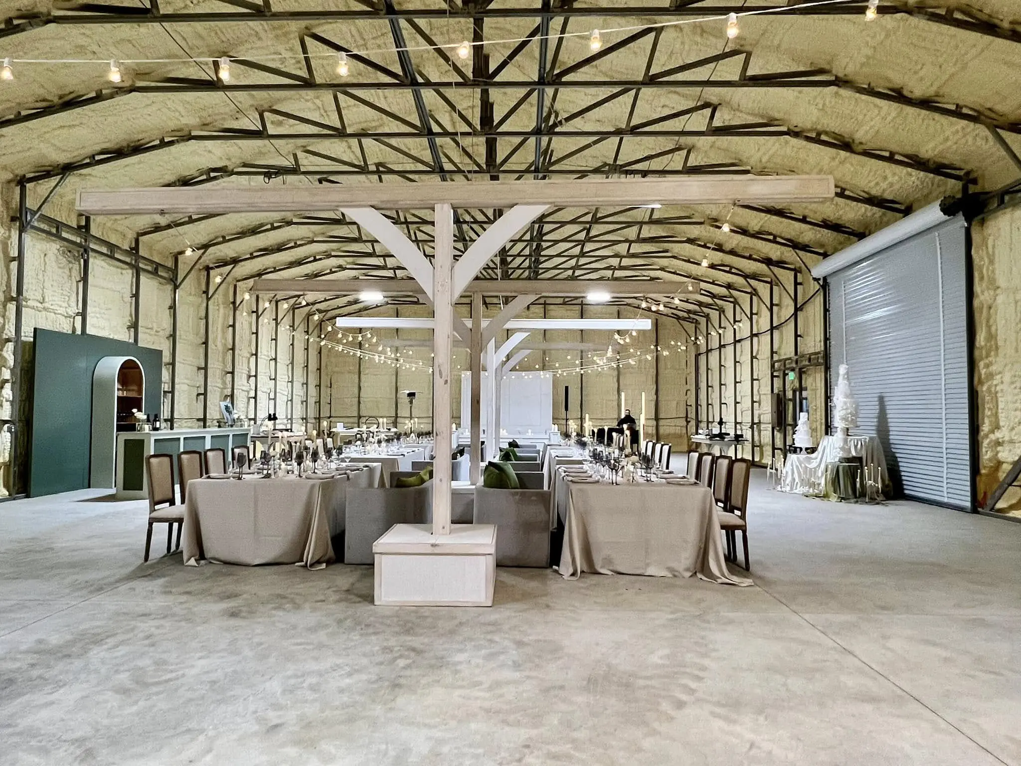 Insulated steel building interior arranged for an event with dining tables and string lights