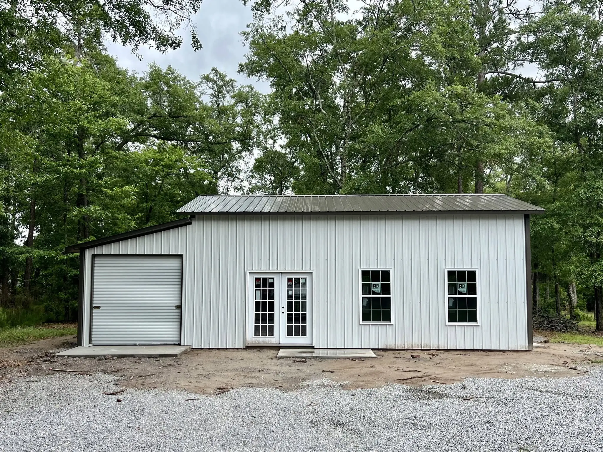 White steel building with black roof, windows, double doors, and an adjoining garage bay