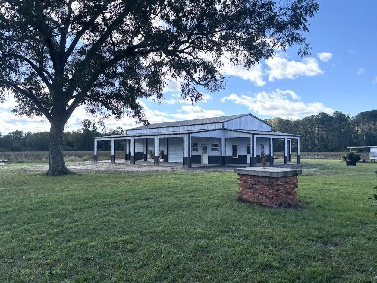 White steel barn with dark trim, multiple roll-up doors, and covered porches